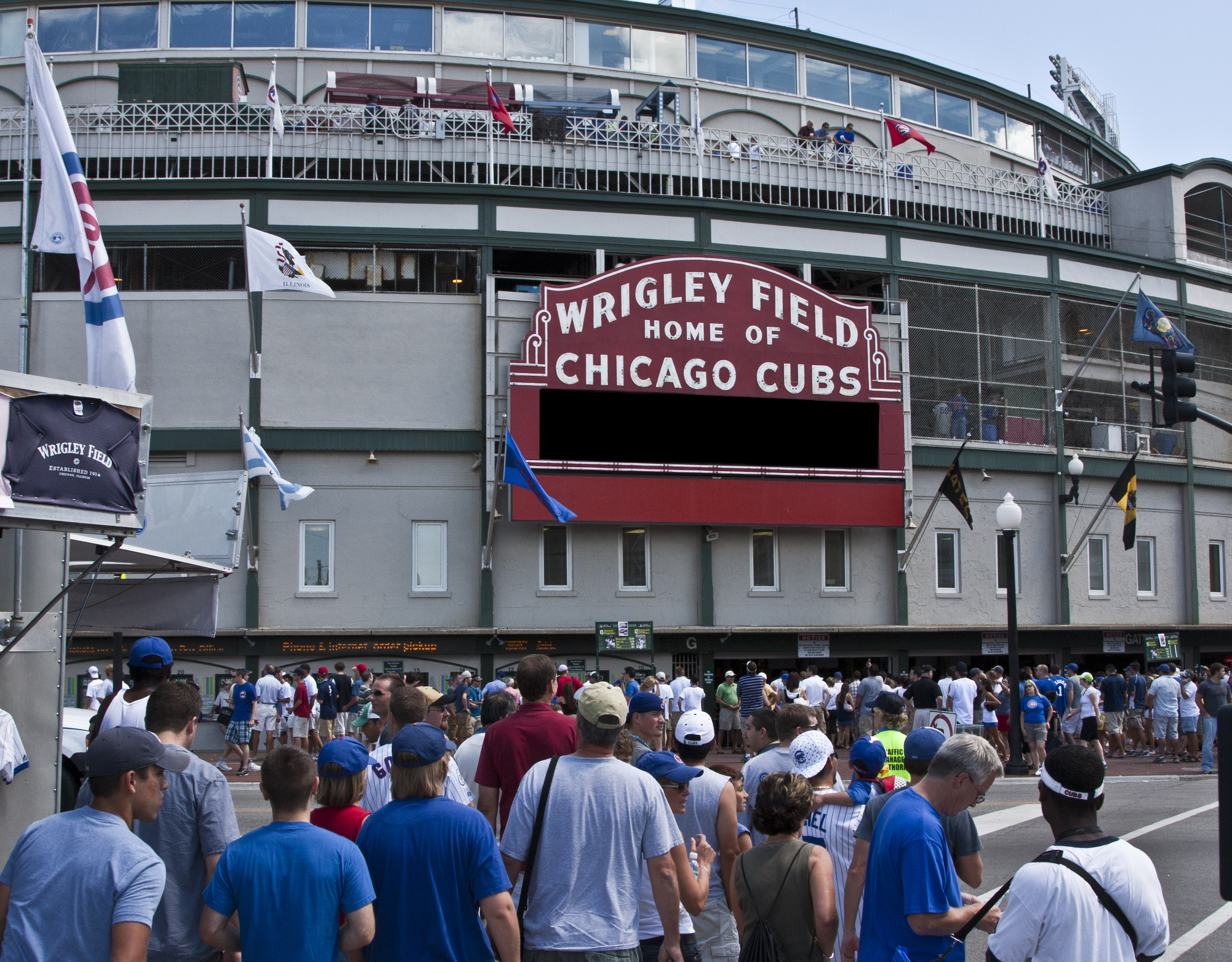 A large crowd of people waiting outside Wrigley Field, home of the Chicago Cubs, with many wearing baseball caps and team jerseys