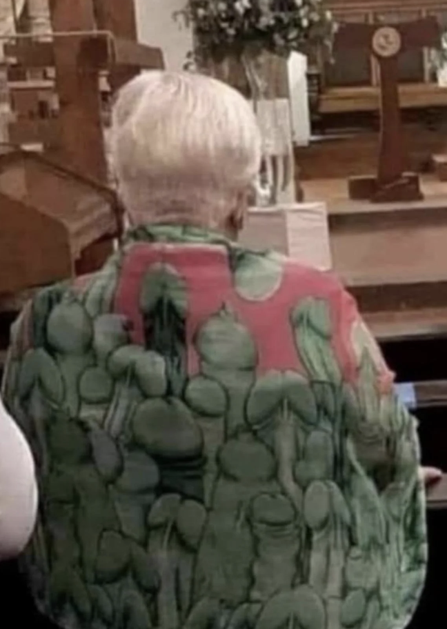An older individual with short white hair is seen from the back, wearing a green and pink patterned shirt, seated in what appears to be a church or religious setting