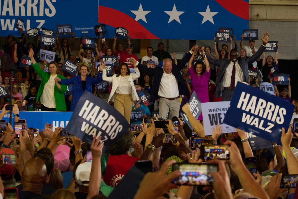 Kamala Harris and supporters on a stage at a rally holding hands