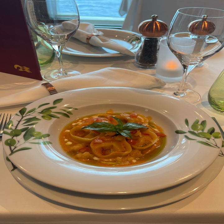 A plate of pasta with tomato sauce and basil, elegantly set on a white-clothed dining table with fine glassware and tableware