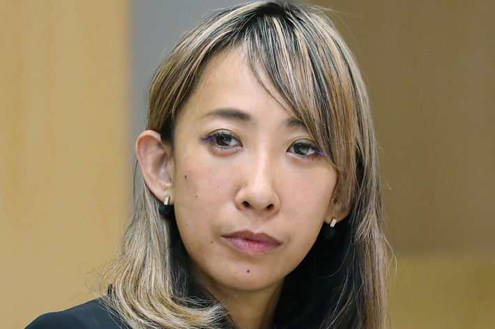 女性がインタビューに答えている様子。黒いジャケットと花柄のシャツを着用。