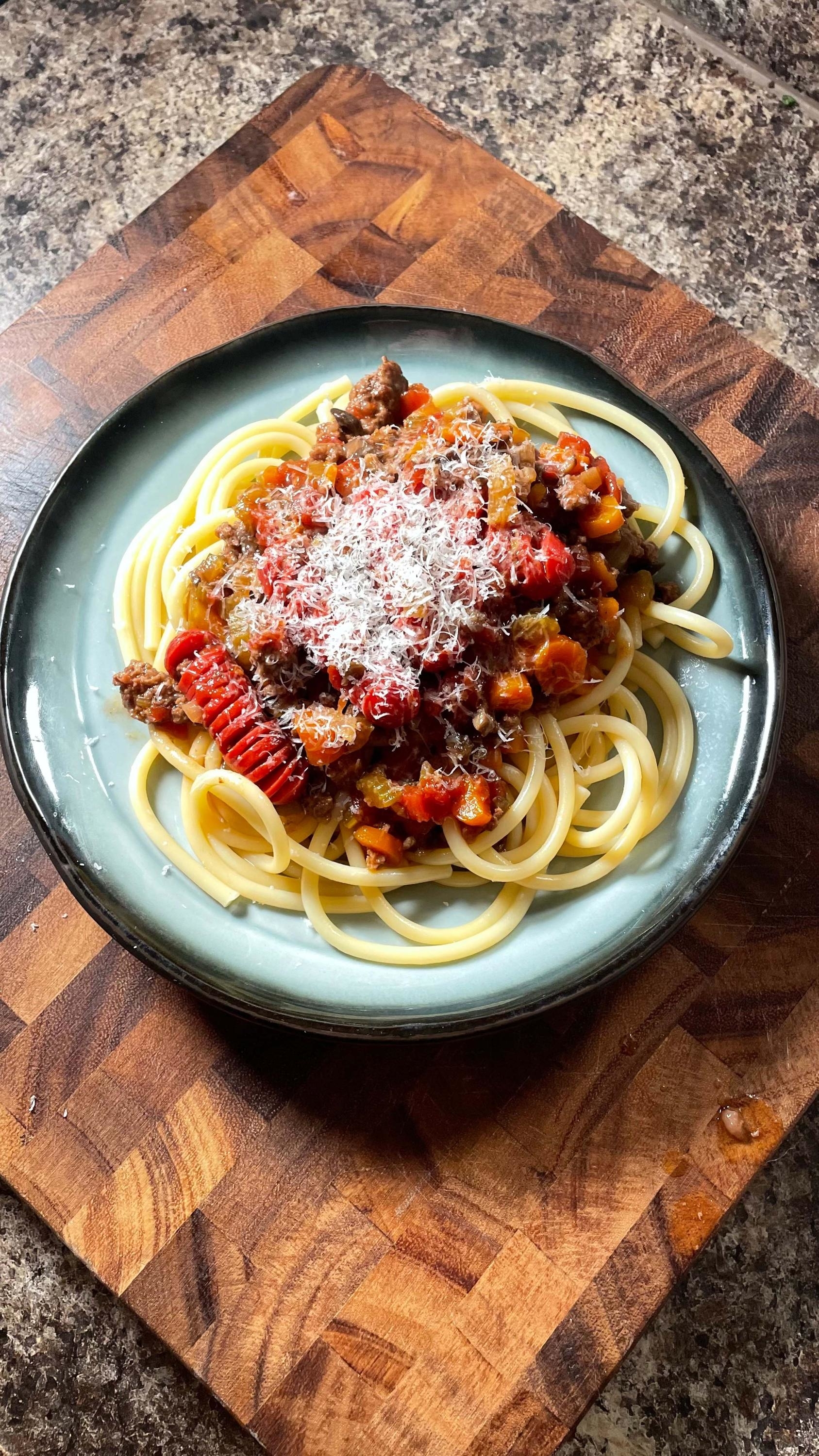 A plate of spaghetti topped with a homemade meat sauce and grated cheese, served on a wooden cutting board