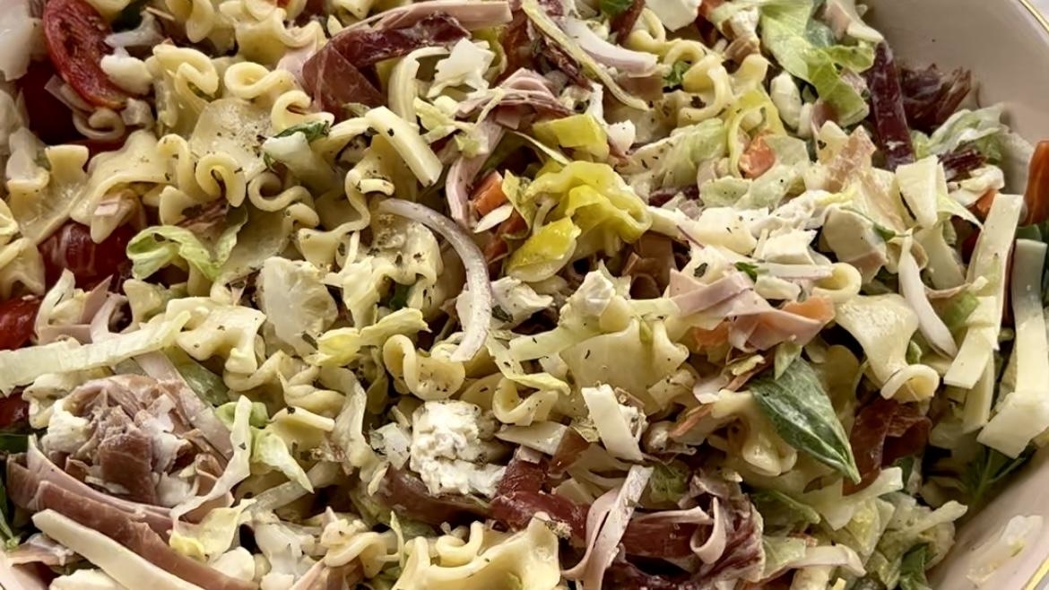 A close-up of a pasta salad mixed with assorted ingredients including sliced meats, vegetables, and cheese