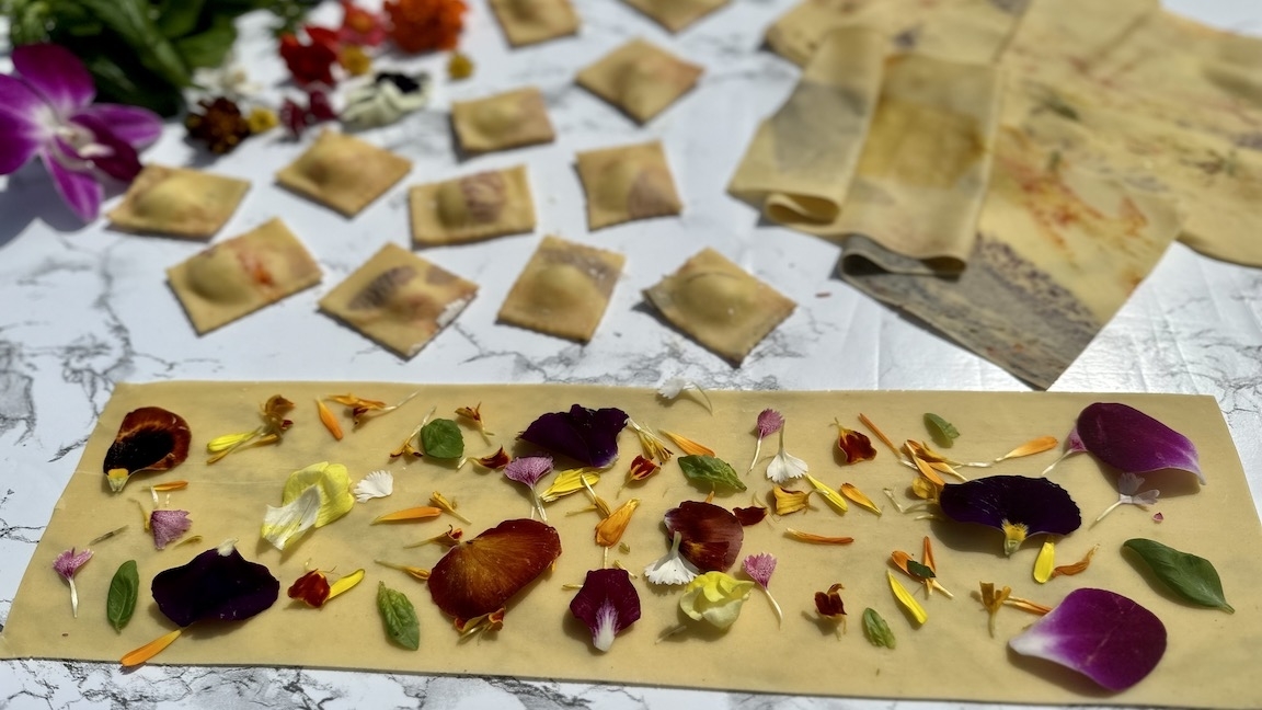 Ravioli pasta decorated with assorted flower petals and herbs on a marble surface