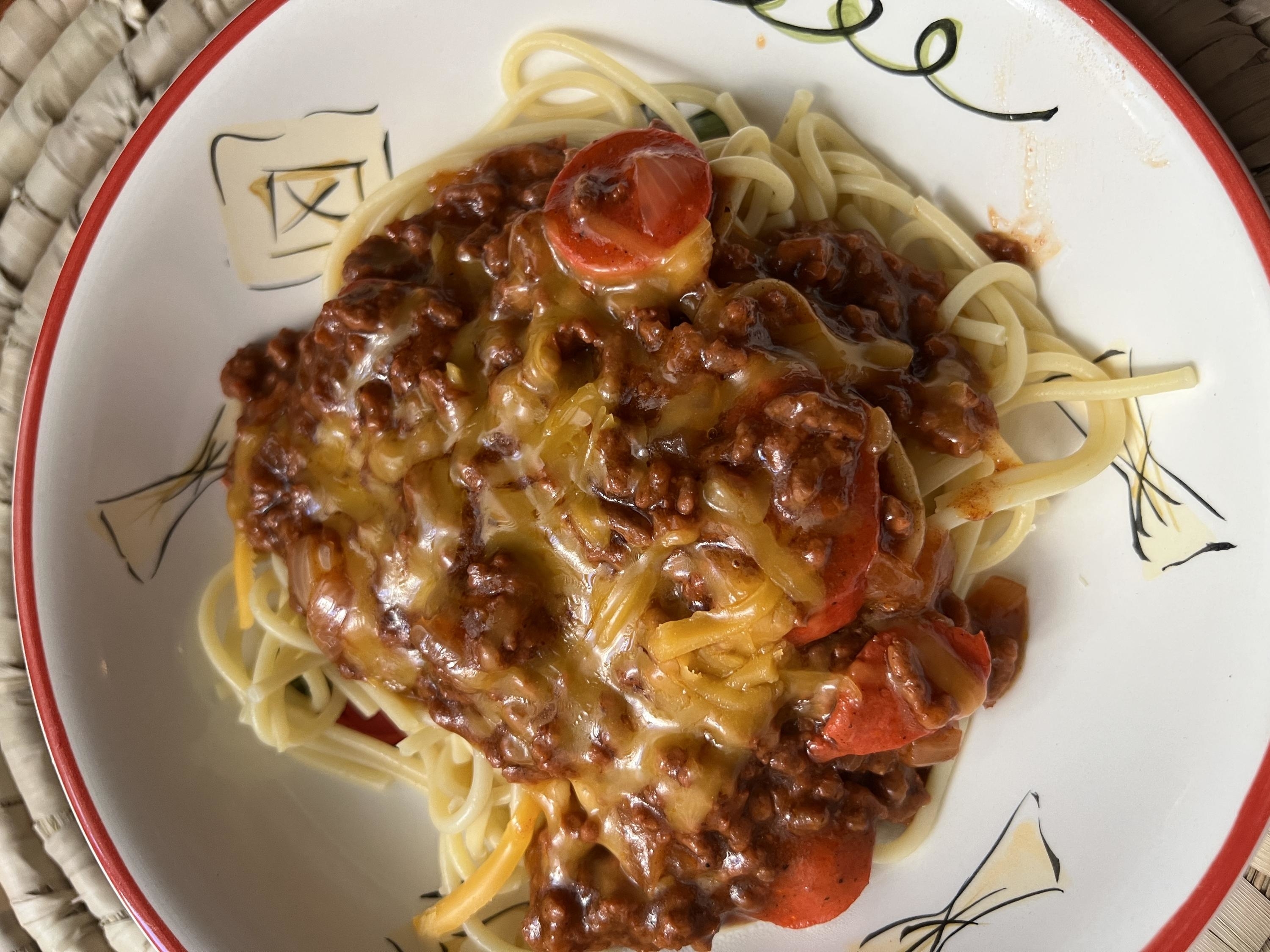 A plate of spaghetti topped with beef bolognese sauce, cherry tomatoes, and melted cheese
