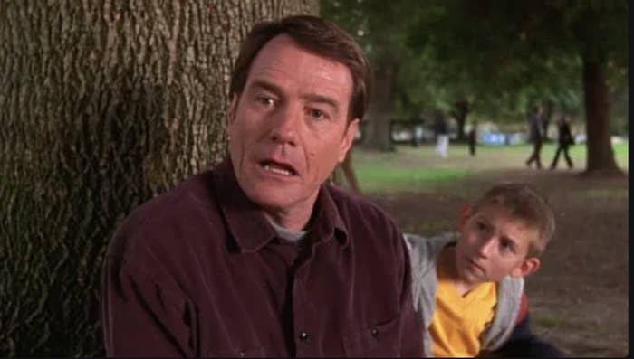 Bryan Cranston and Frankie Muniz sit by a tree in a park, both appearing concerned or surprised