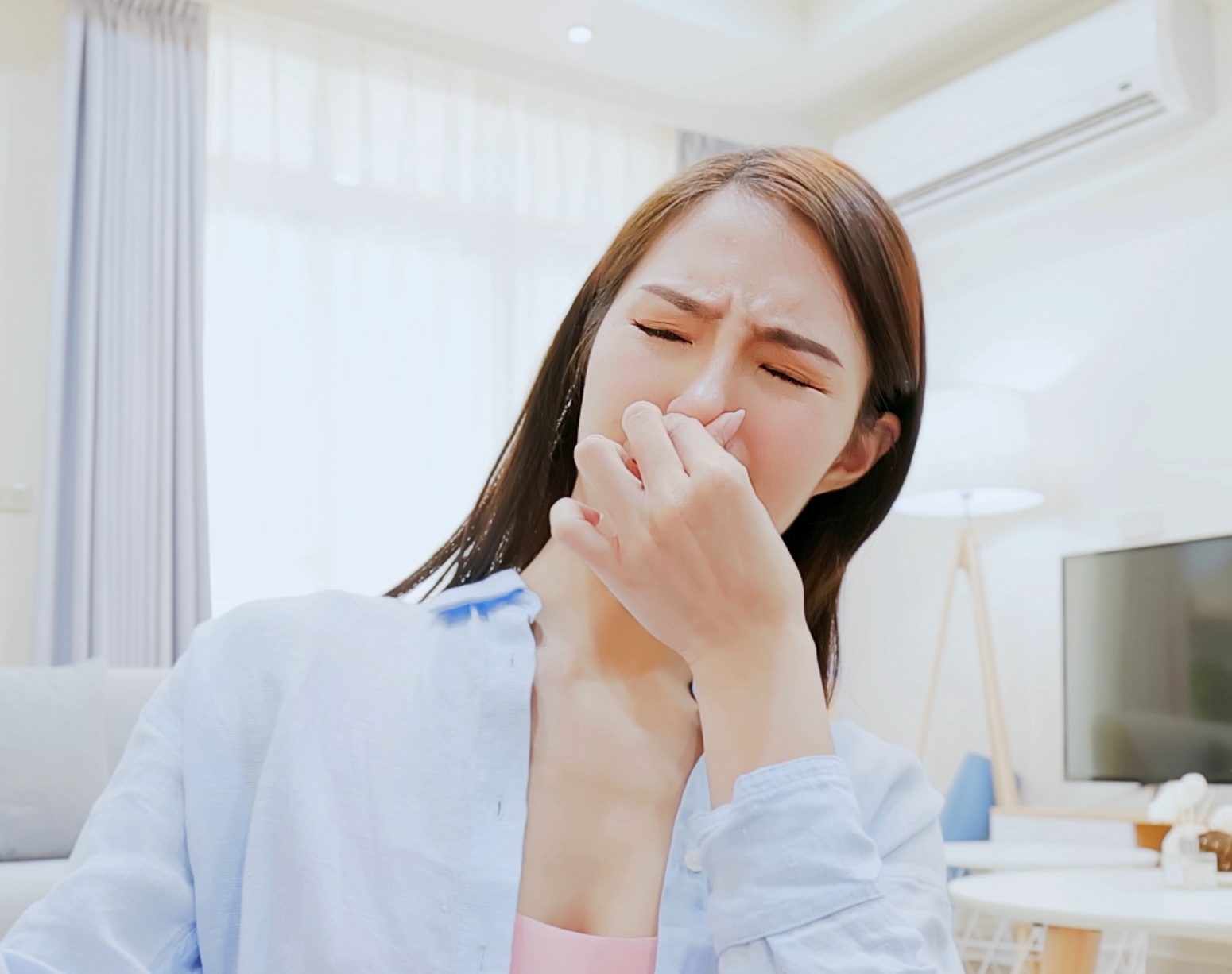 女性が室内で鼻をつまんで苦しそうな表情をしている。