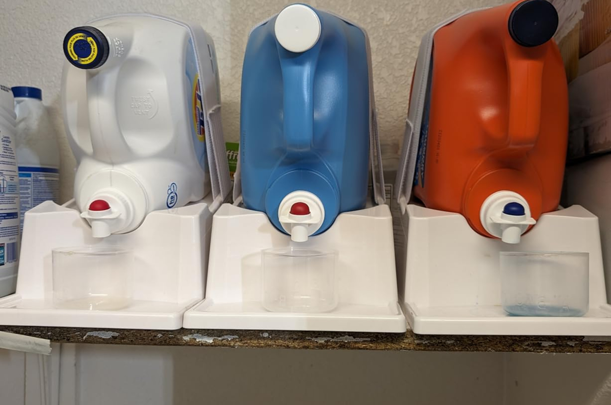 Three large detergent containers on dispensers, placed on a shelf in a laundry room