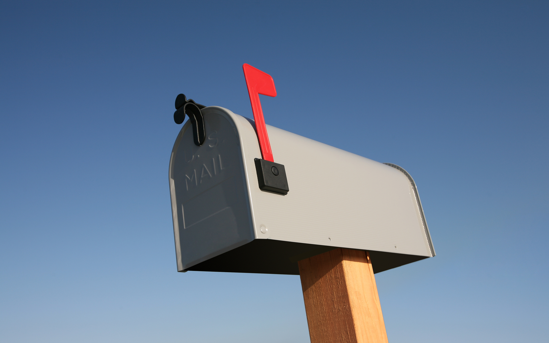 A single metal mailbox on a wooden post with its red flag up against a clear blue sky