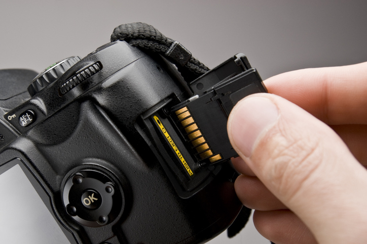 A person's hand is inserting a memory card into a digital camera