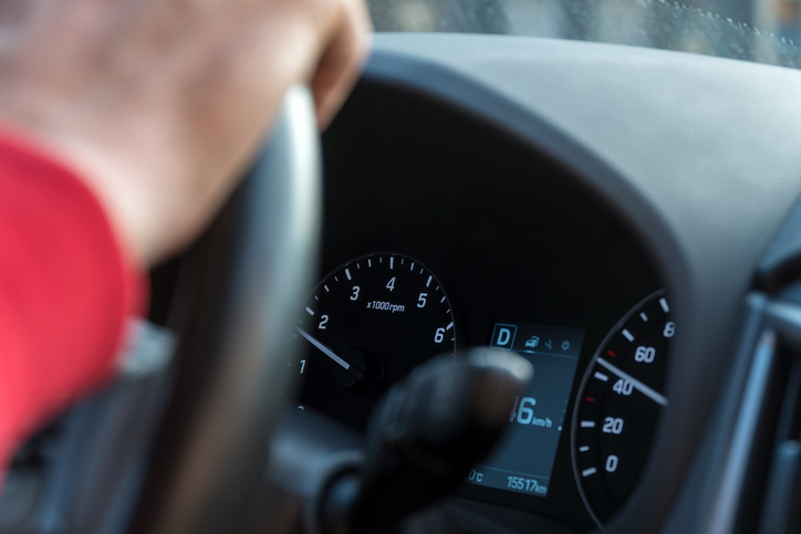 Close-up of a person's hand on a car steering wheel, focusing on the car's speedometer and dashboard