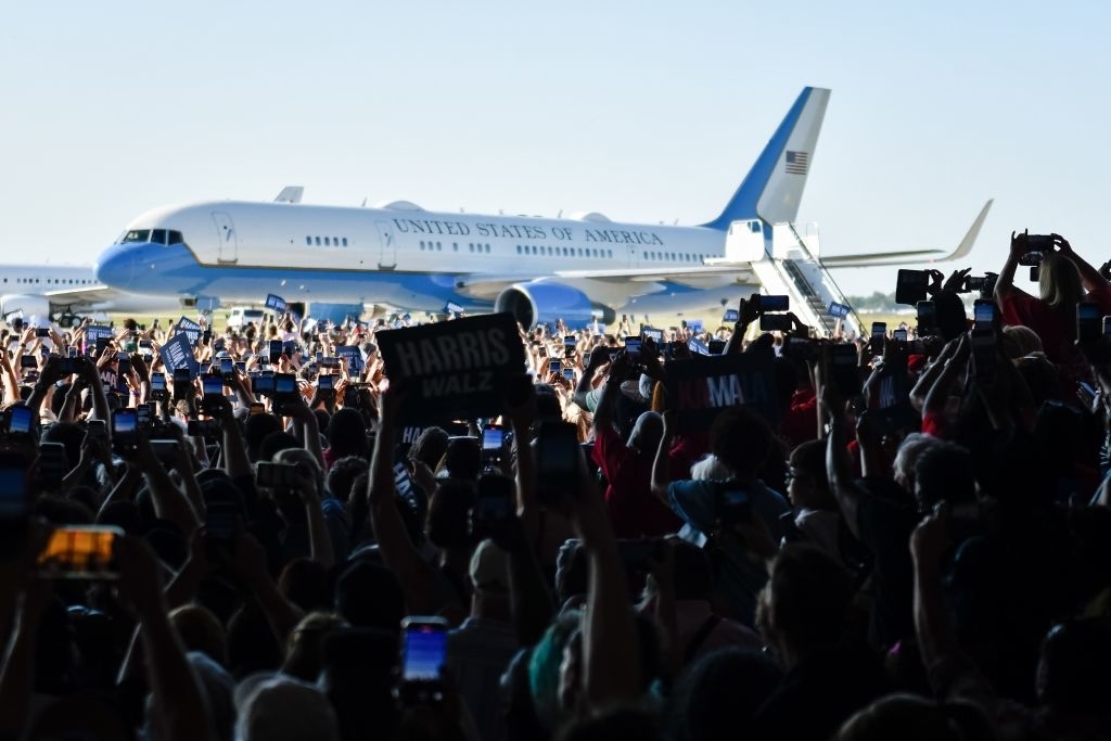 A crowd attends a Kamala Harris rally with a United States of America government plane is seen in the background on the runway