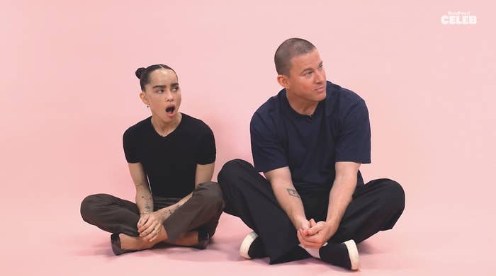 Zoe Kravitz and Channing Tatum sit casually on the floor against a light backdrop, with Zoe yawning and Channing looking away, both wearing relaxed, simple outfits