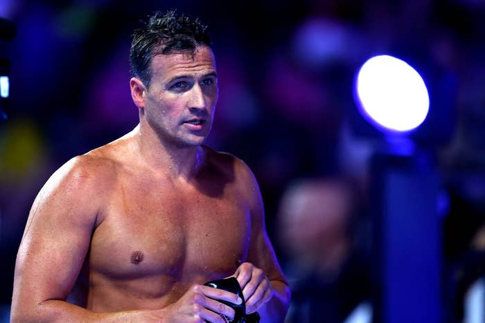 Ryan Lochte stands shirtless, holding his swim gear, after a swimming event