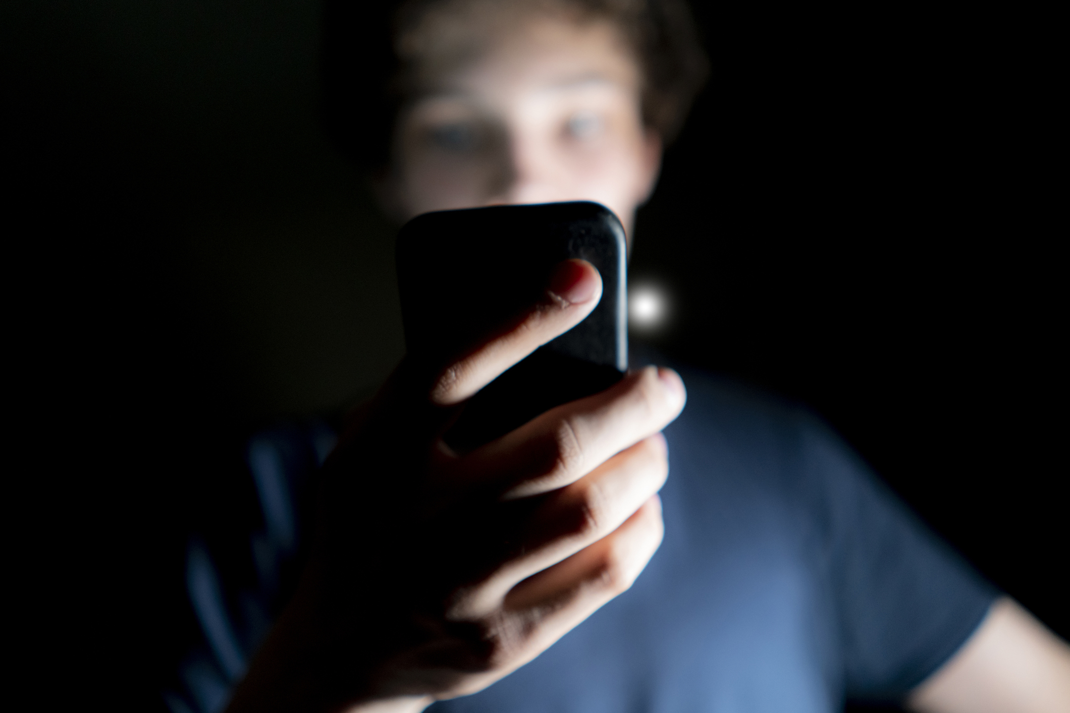 Person looking at their phone screen in a dark setting, face somewhat obscured by the light from the phone
