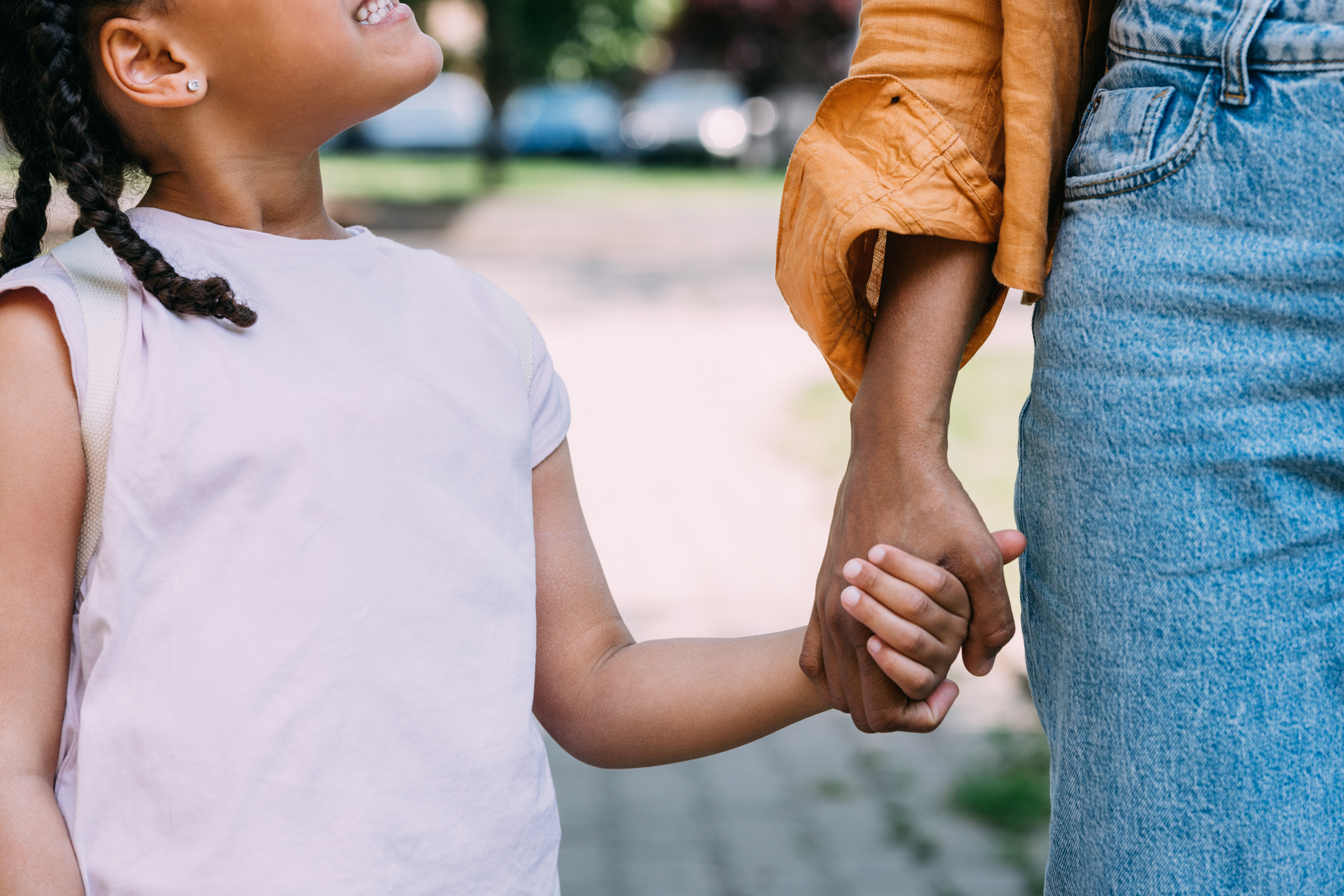 A young child holding hands with an adult outdoors, both smiling and walking together