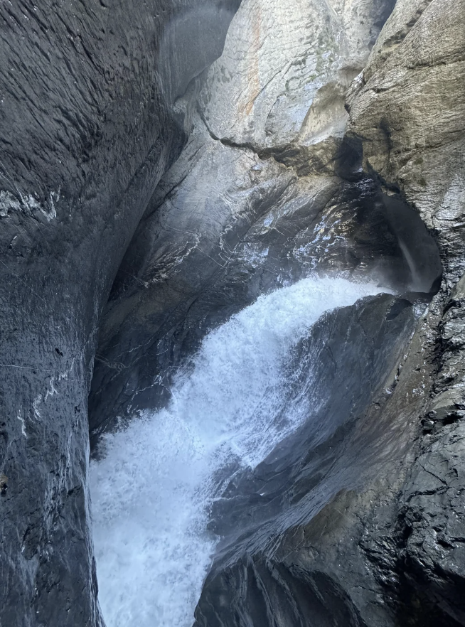 A powerful waterfall cascades between tall, rugged rocks in a narrow gorge, creating mist and rushing water below