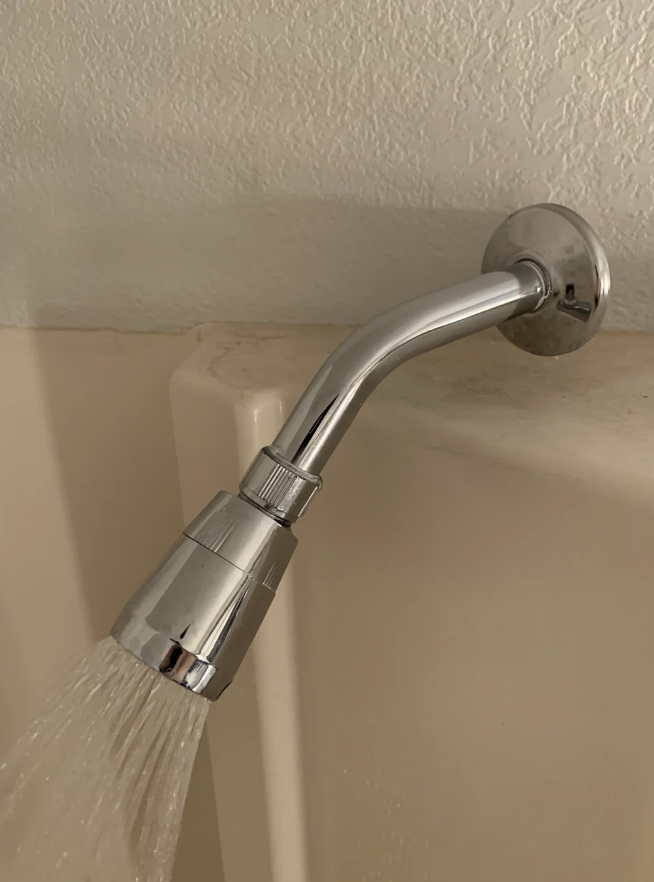 Close-up image of a chrome showerhead attached to a wall, with water flowing from it into a tub