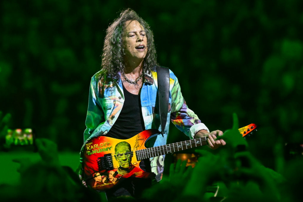 Kirk Hammett playing a guitar on stage, wearing a vibrant, patterned shirt