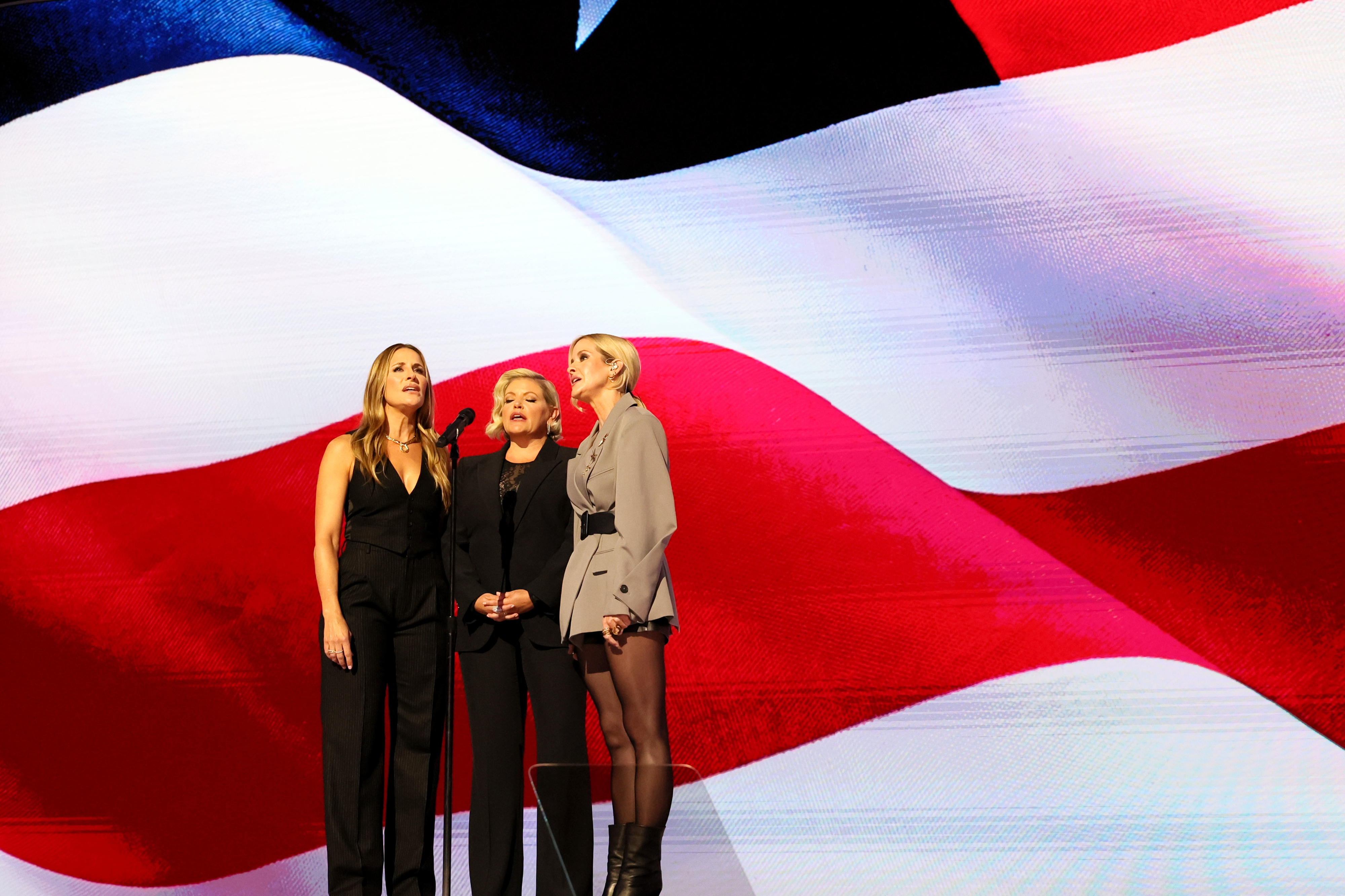 Natalie Maines, Emily Strayer, and Martie Maguire from The Chicks singing on stage with a large American flag backdrop