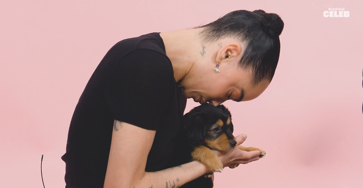 Zoe Kravitz gently cradles a small puppy while seated against a plain background, featured in a Buzzfeed Celeb interview