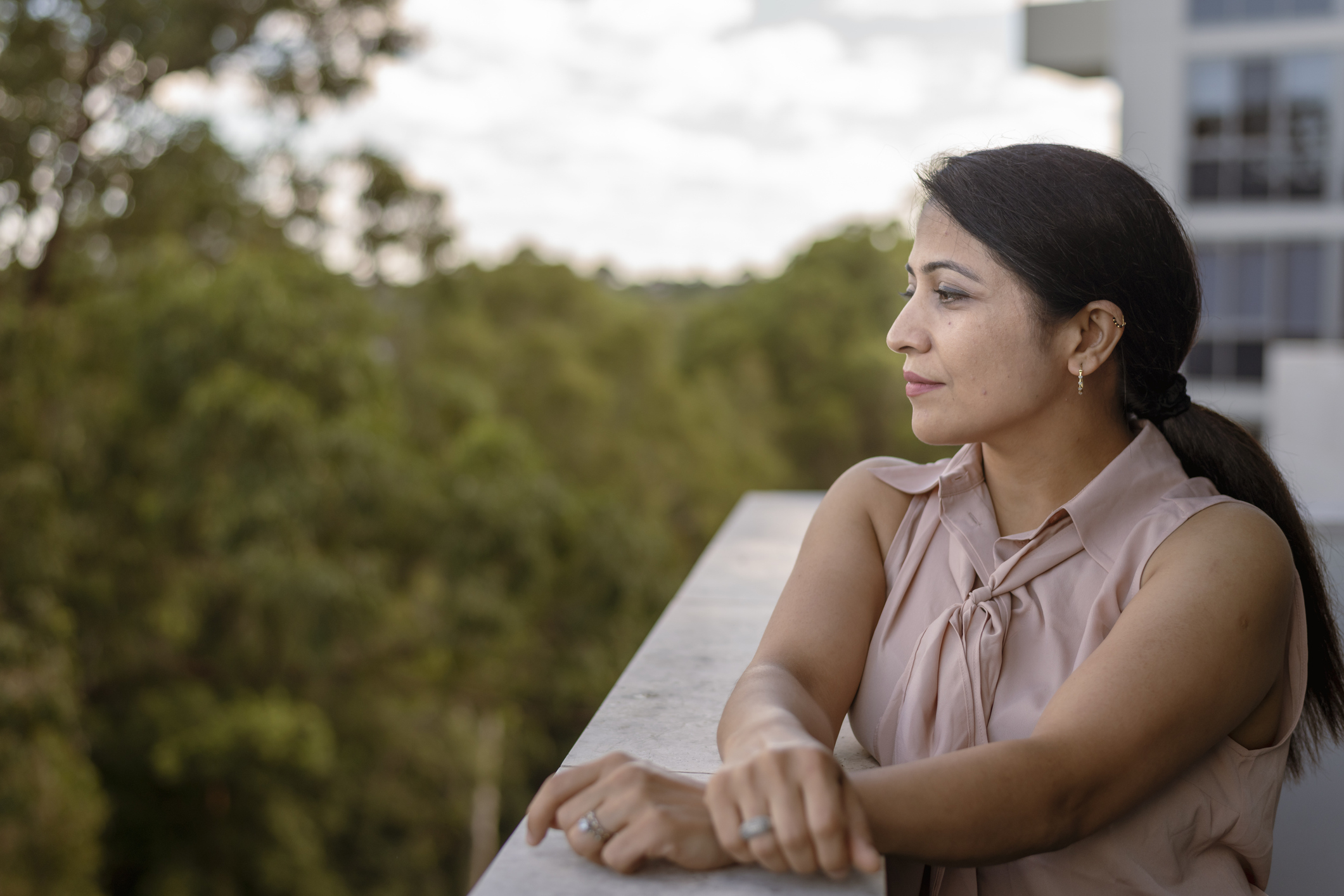 A woman standing on a balcony, gazing into the distance with a thoughtful expression