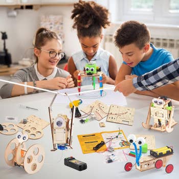 Three children assembling robotic kits connected a table. Various woody robot parts and tools are dispersed out
