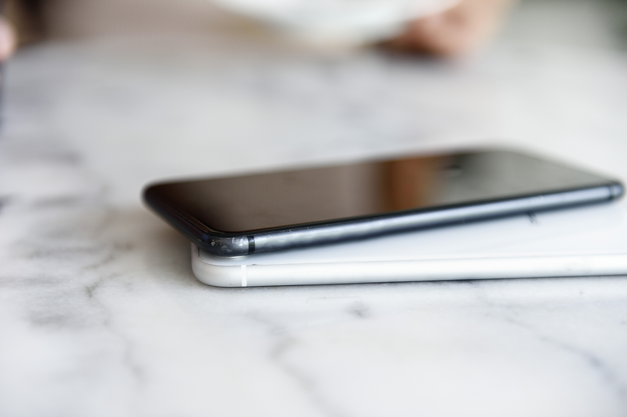 A close-up image of two smartphones stacked on top of each other on a marble table, reflecting the light