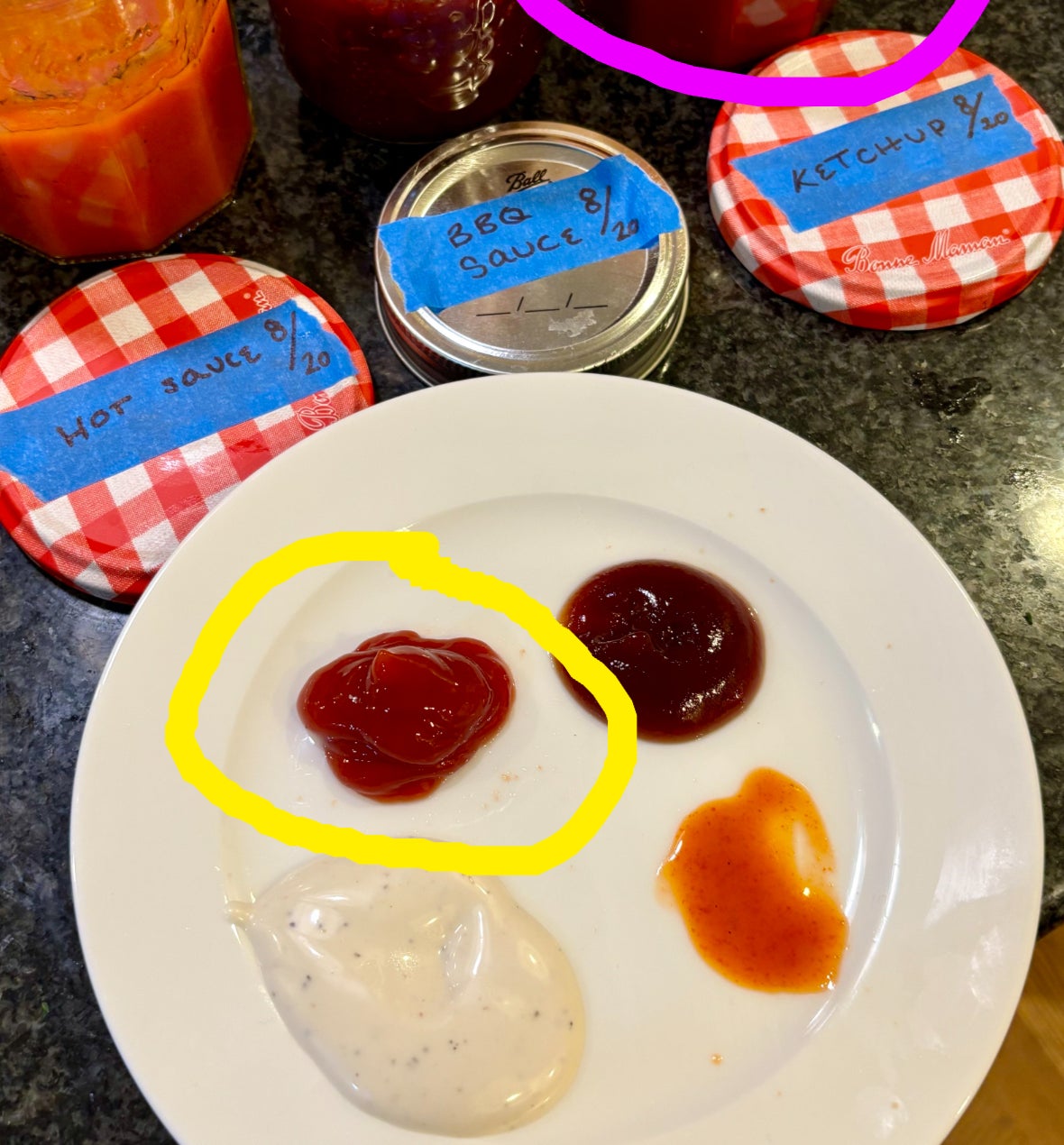 Four jars of homemade sauces (hot sauce, sea sauce, ketchup, and BBQ) with lids labeled in blue tape and a plate displaying samples of each sauce