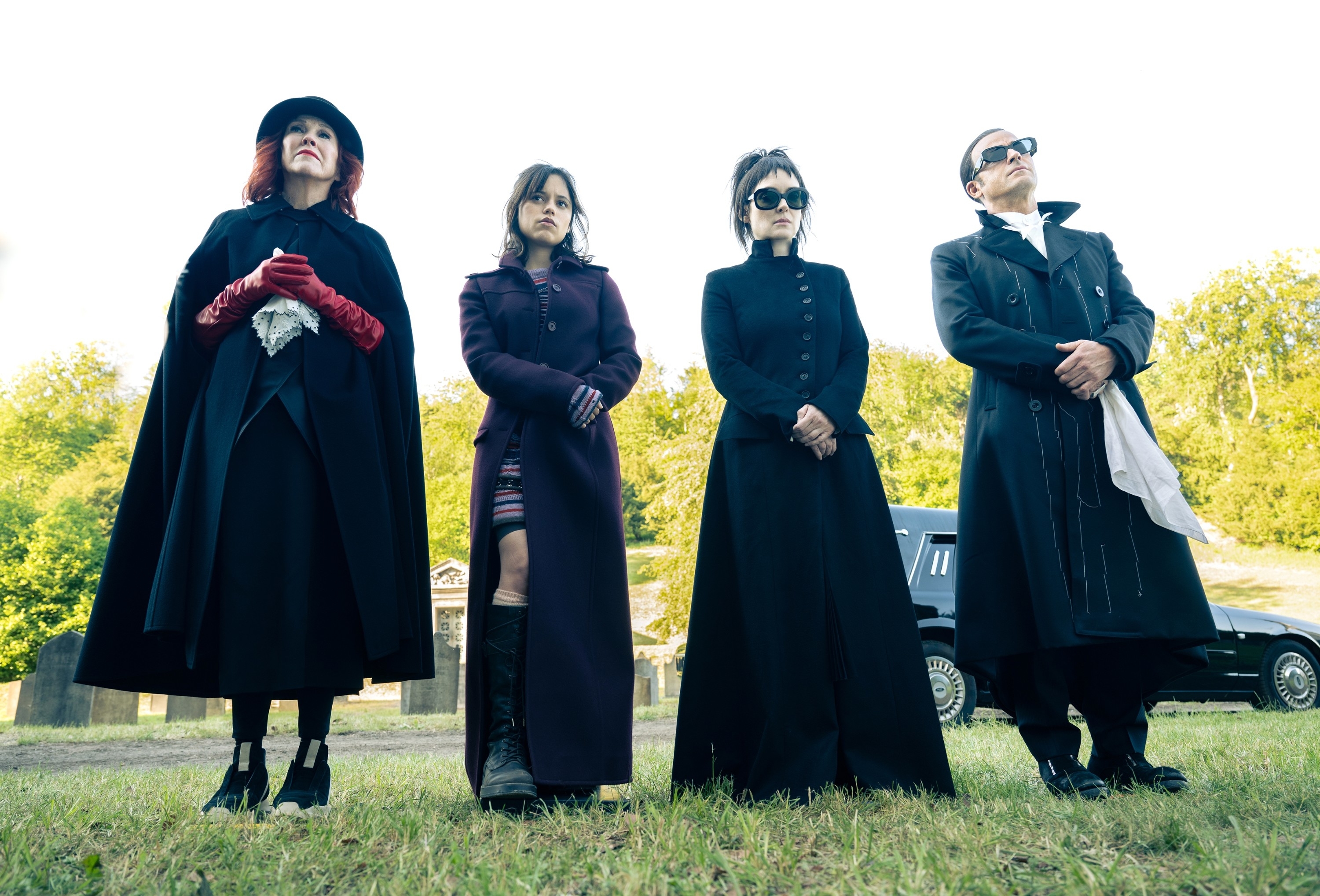 Catherine O'Hara, Jenna Ortega, Winona Ryder, and Justin Theroux dressed in gothic attire, standing outdoors in a scene from &quot;Wednesday&quot;