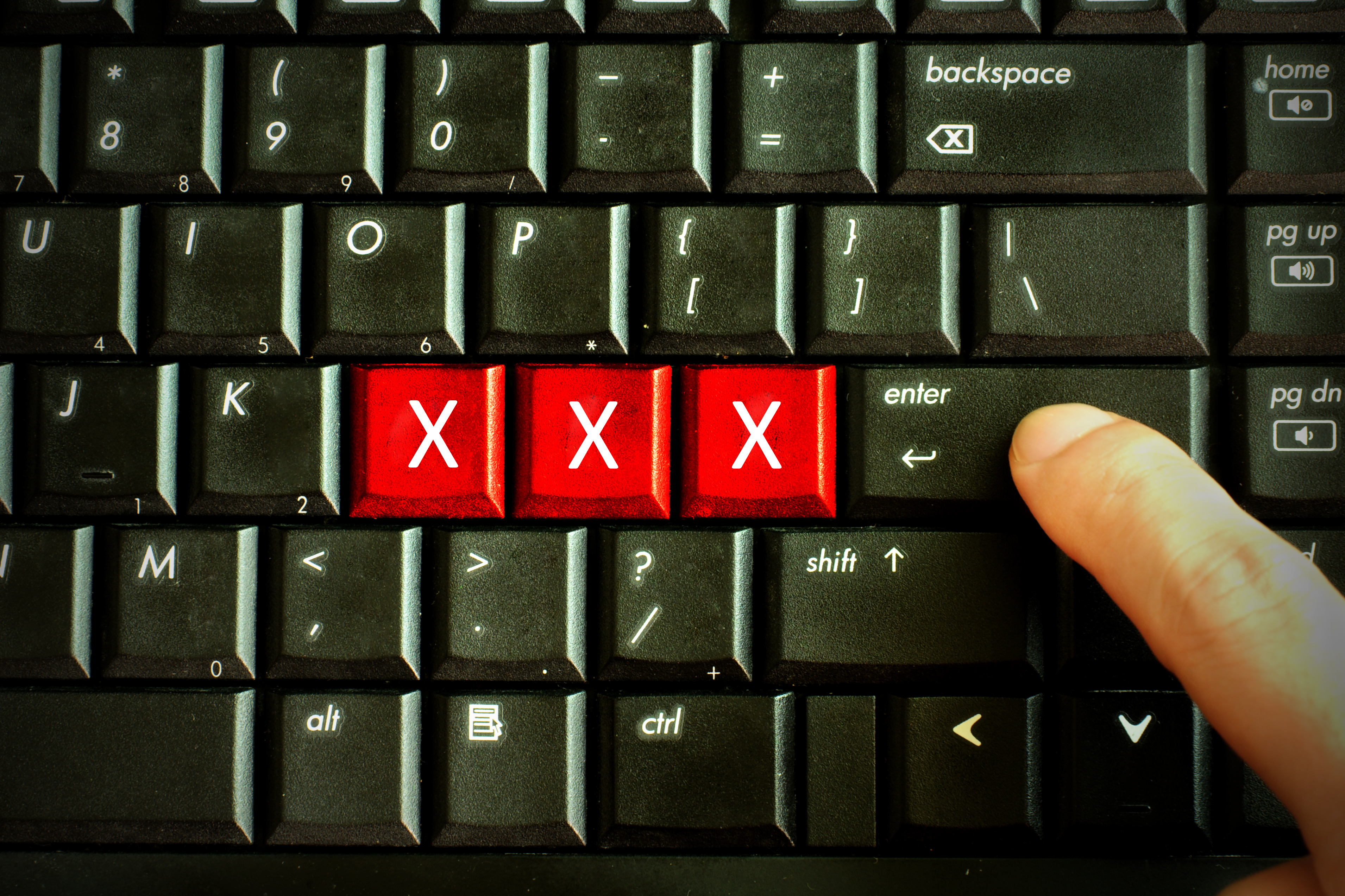 A close-up image of a keyboard with the letters &quot;XXX&quot; highlighted in red and a finger pressing the enter key, implying adult or explicit content
