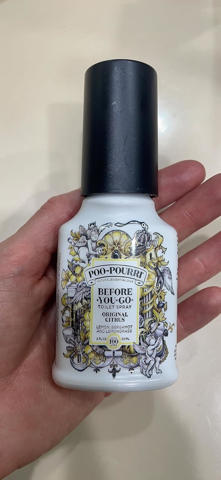 網頁設計 Hand holding a Poo-Pourri Before You Go toilet spray bottle, original citrus scent. Decorative label includes floral and bird illustrations