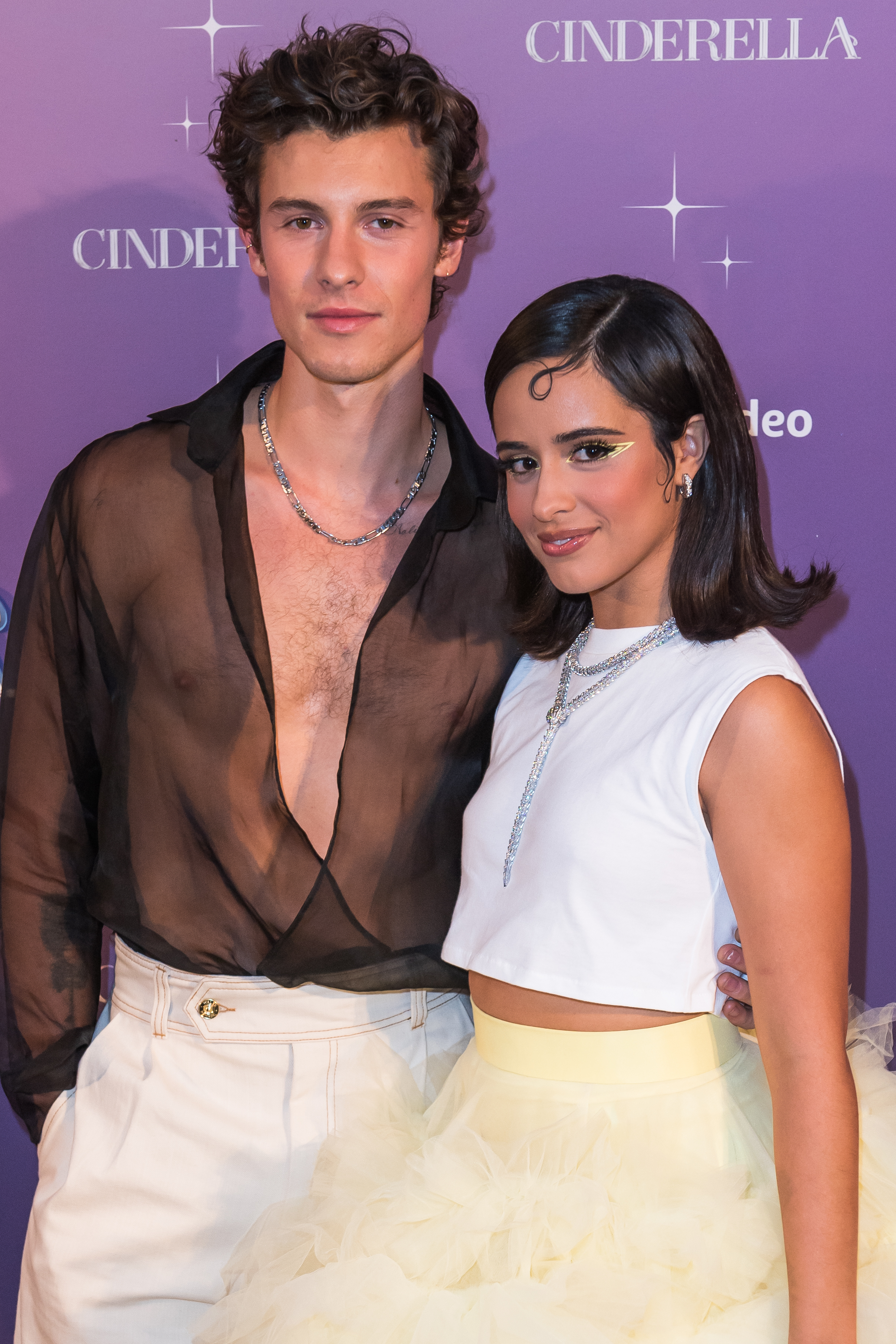 Shawn Mendes and Camila Cabello at the "Cinderella" event. Shawn wears a sheer black shirt and white pants, while Camila wears a white crop top and tulle skirt