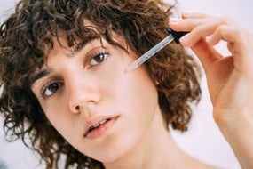 Woman with curly hair applying serum to their face with a dropper