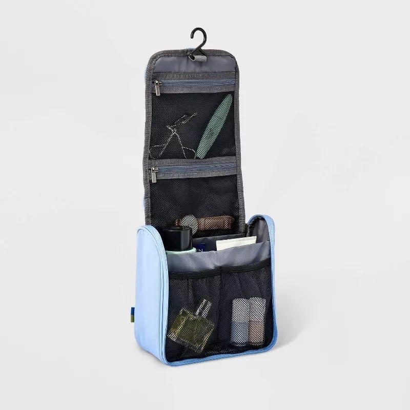 Hanging toiletry bag with various compartments holding travel-size personal care items like a razor, toothbrush, bottles, and a folded cloth