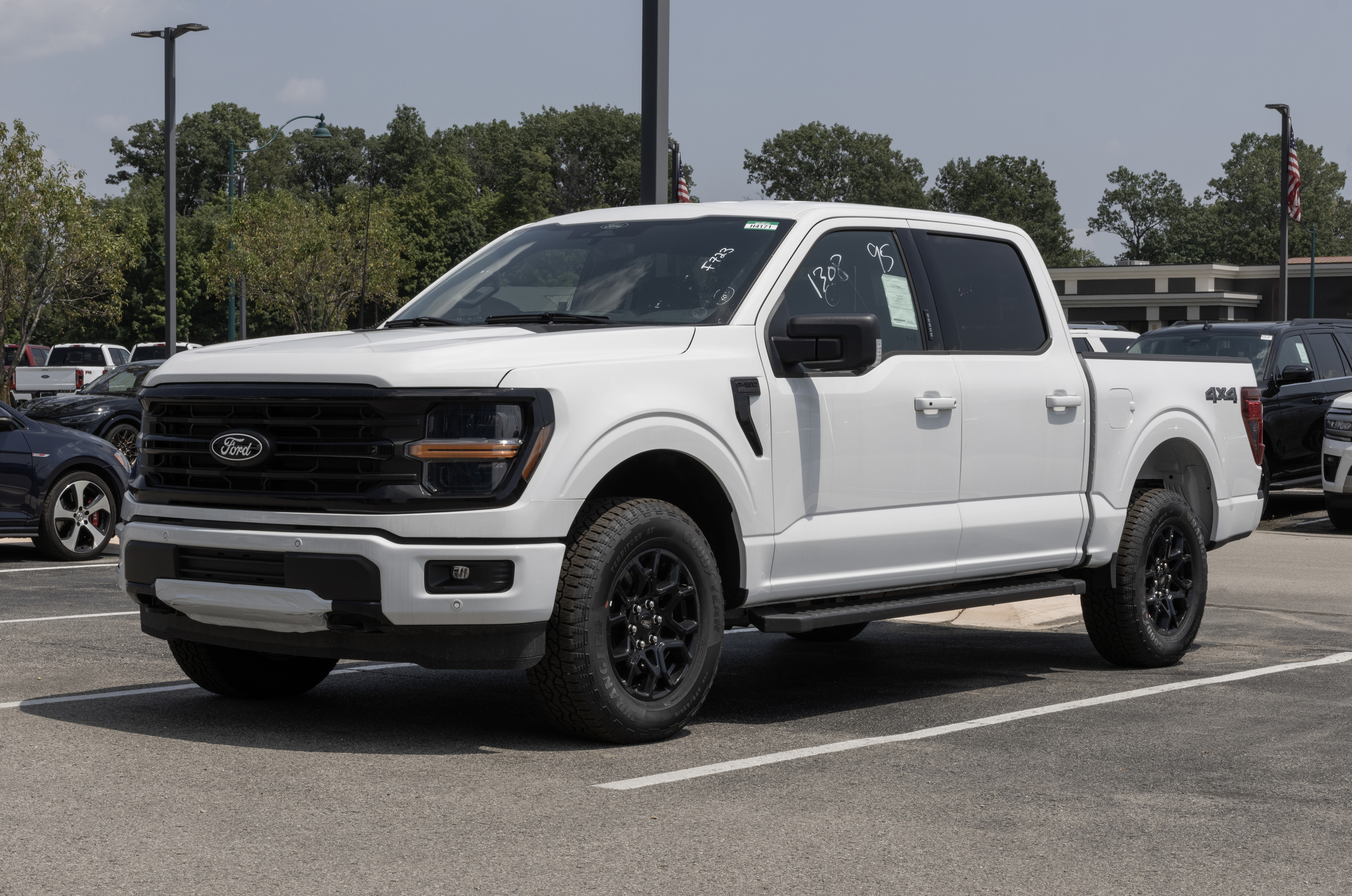 A white Ford F-150 truck is parked in an outdoor parking lot with several other vehicles in the background