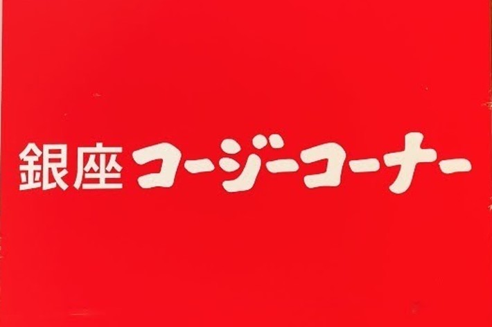 A sign on a brick wall reads “銀座コージーコーナー” (Ginza Cozy Corner) with a smaller block of text below it that is not fully visible