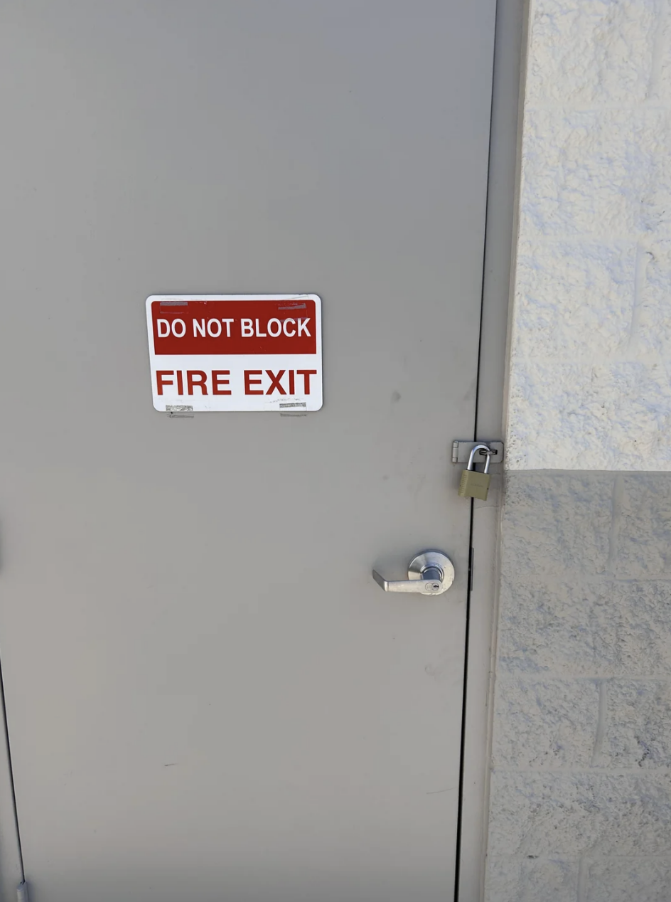 A grey door with a sign that says &quot;Do Not Block Fire Exit;&quot; the door is locked with a padlock