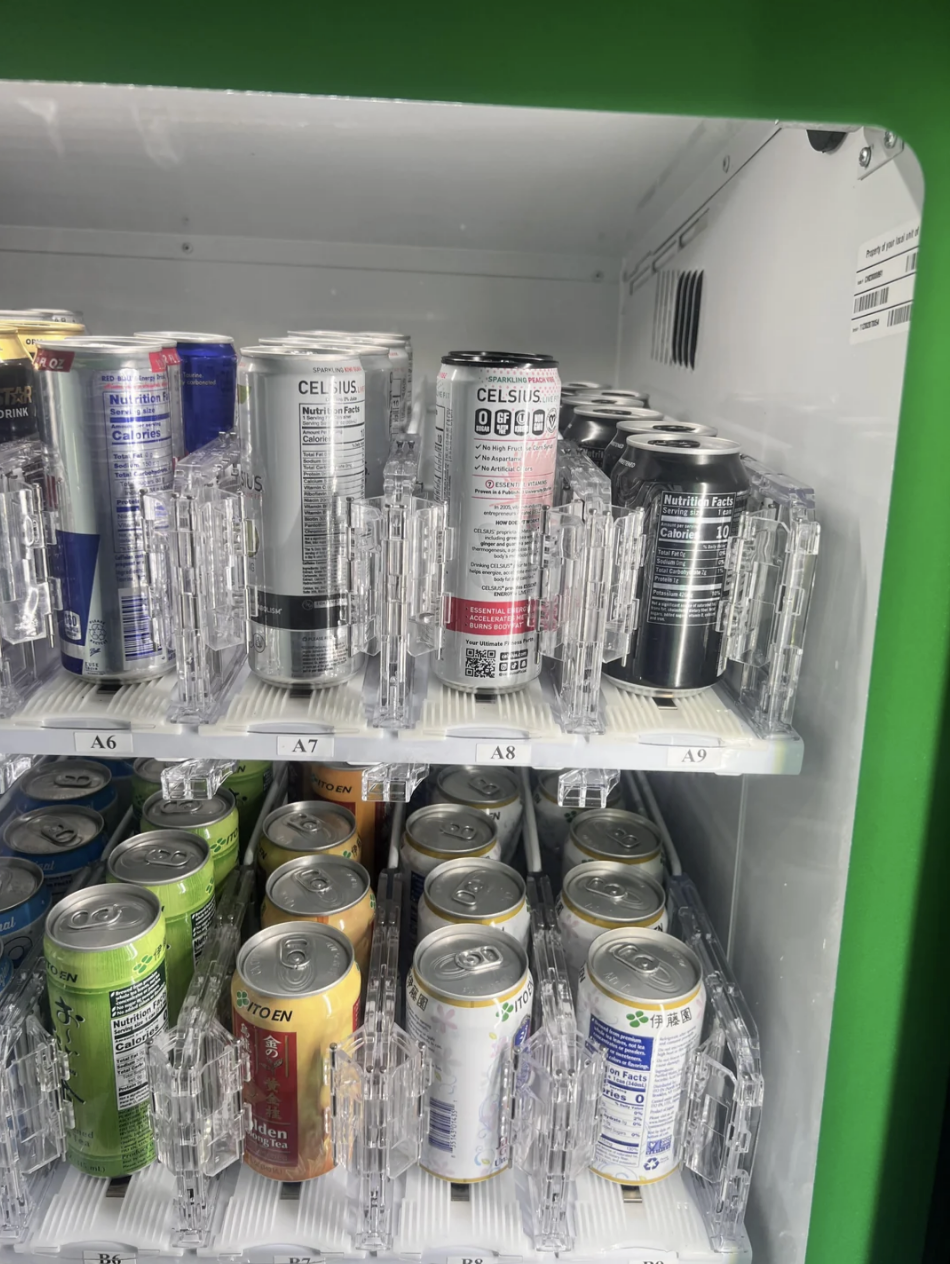 Cans of various energy drinks, including Celsius and other brands, are displayed inside a vending machine turned around so you can't see the labels