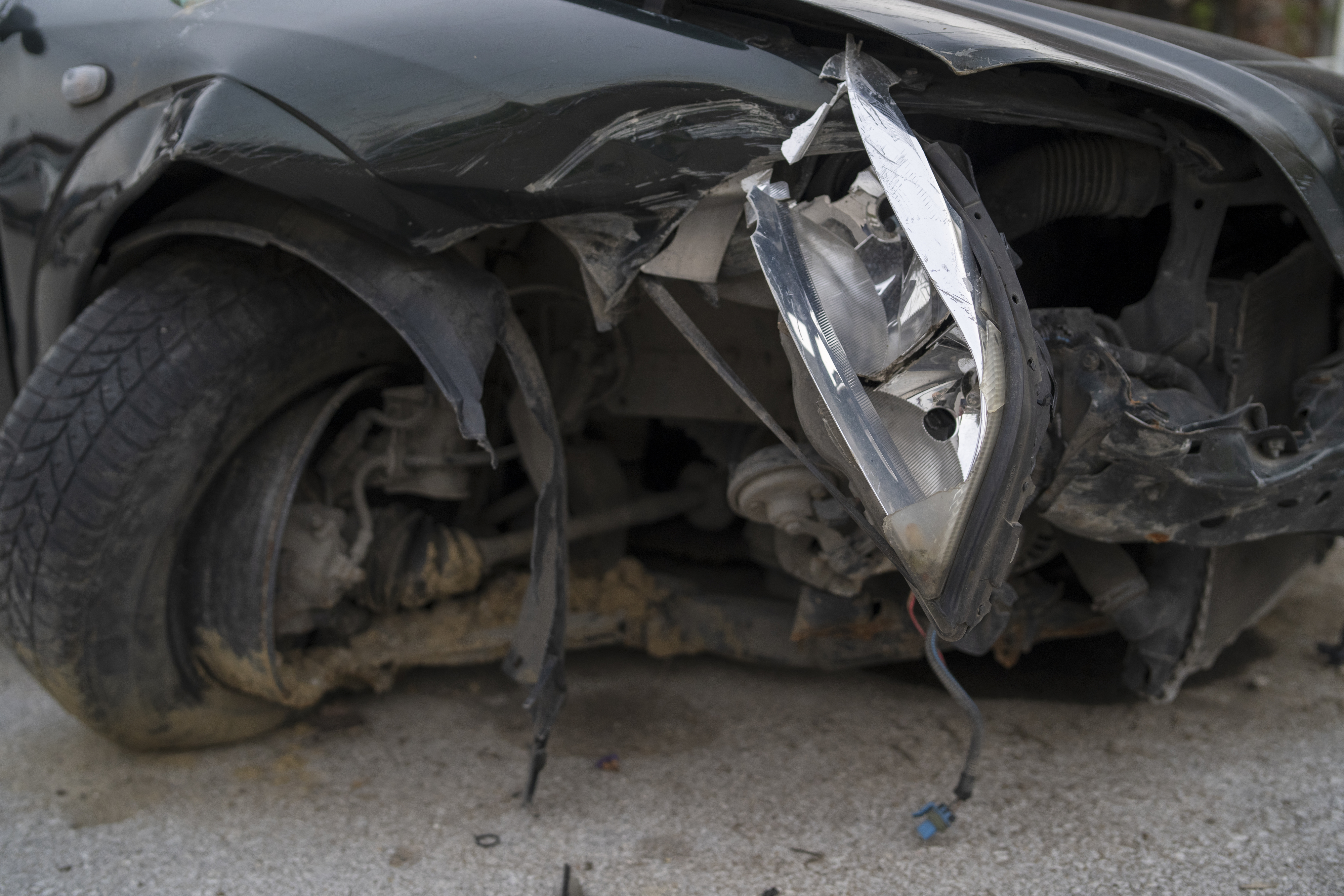 Close-up of a heavily damaged car with a broken headlight, bent metal, and exposed inner workings after an accident