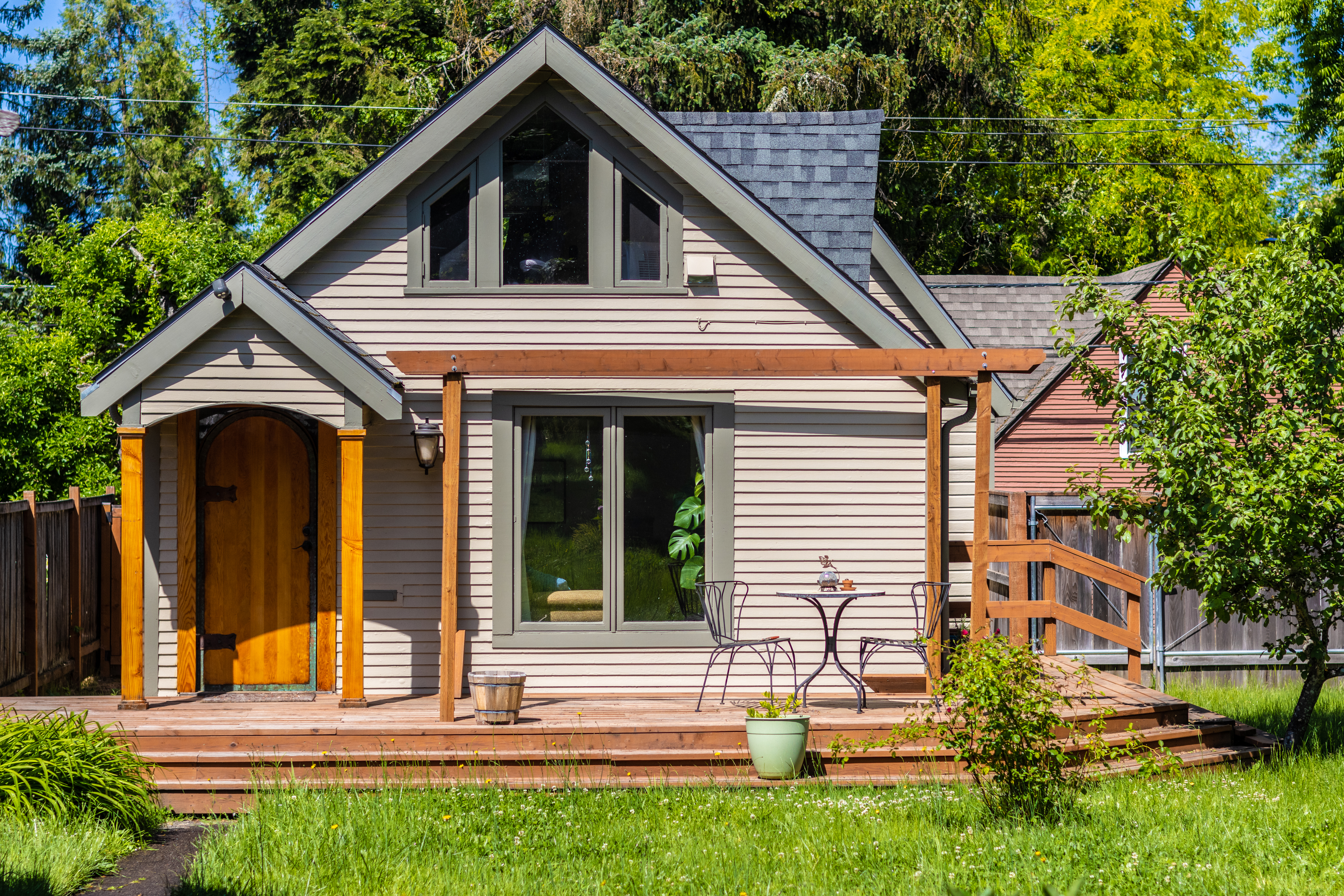A cozy house with a front porch, table and chairs. The surrounding area has greenery and trees