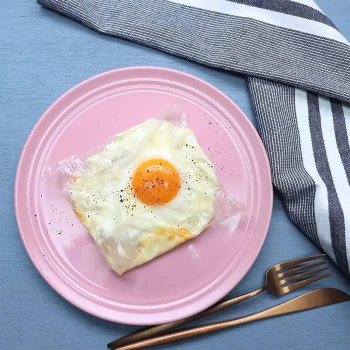 ピンクのお皿に盛り付けられた目玉焼きのガレットと、隣に置かれた銀色のフォークとナイフ。背景に青い布。