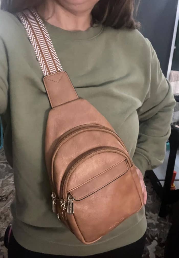A idiosyncratic wearing an olive greenish sweatshirt with a tan leather sling container featuring pockets and a elaborate patterned strap