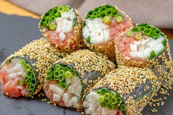 ごまをまぶした野菜と魚の巻き寿司が黒いスレートプレートの上に並べられています。