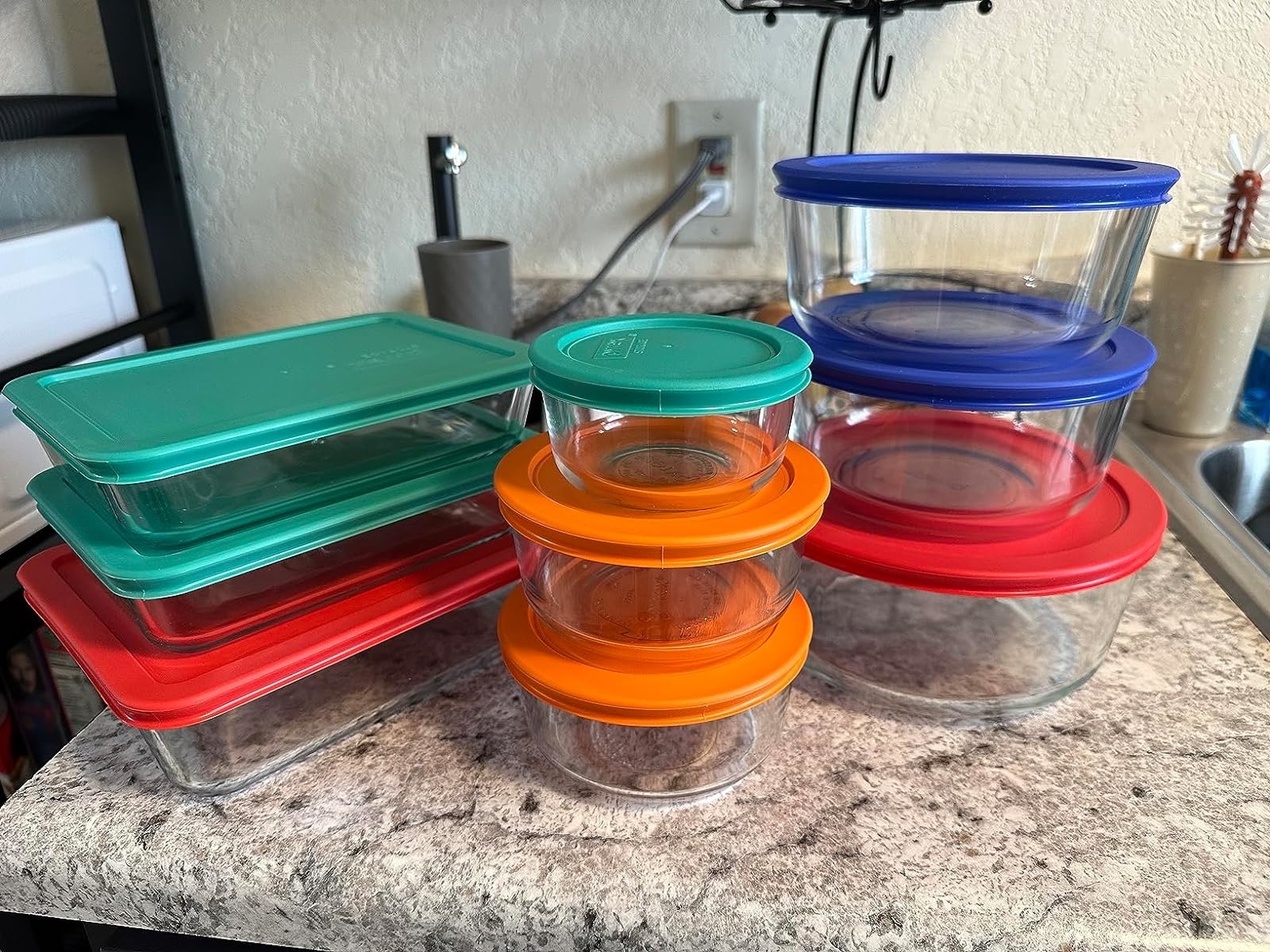 Various sizes of glass food storage containers with colorful lids, arranged on a kitchen countertop