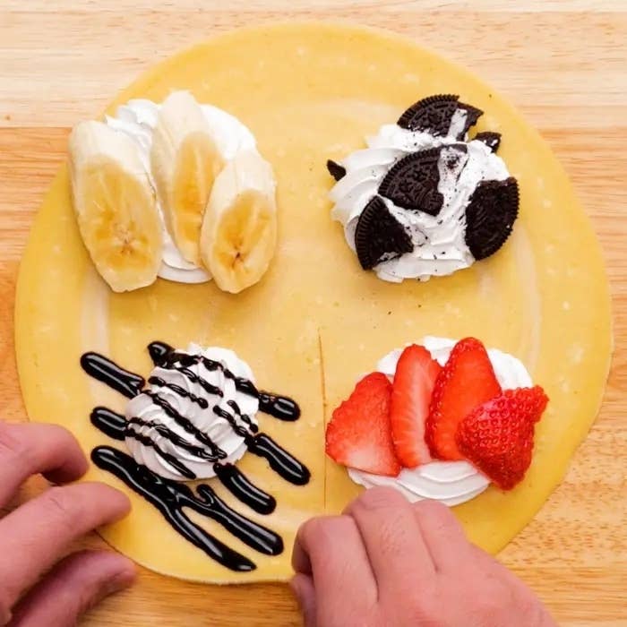 手がバナナ、オレオクッキー、苺、生クリームをトッピングしたクレープを持ちながら巻こうとしている画像です。