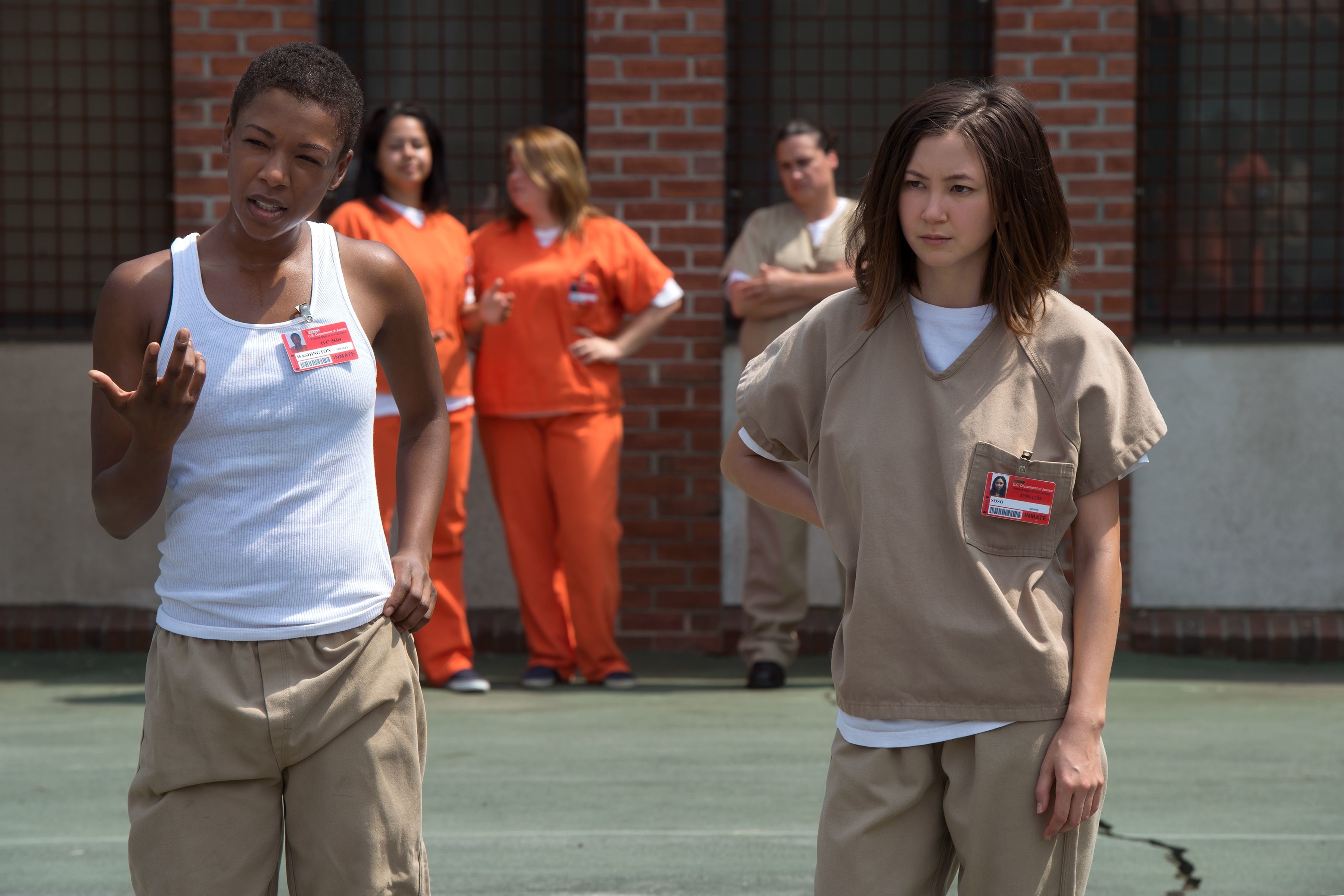 Samira Wiley and Kimiko Glenn in prison uniforms, standing outside with other inmates in the background, scene from &quot;Orange Is the New Black.&quot;