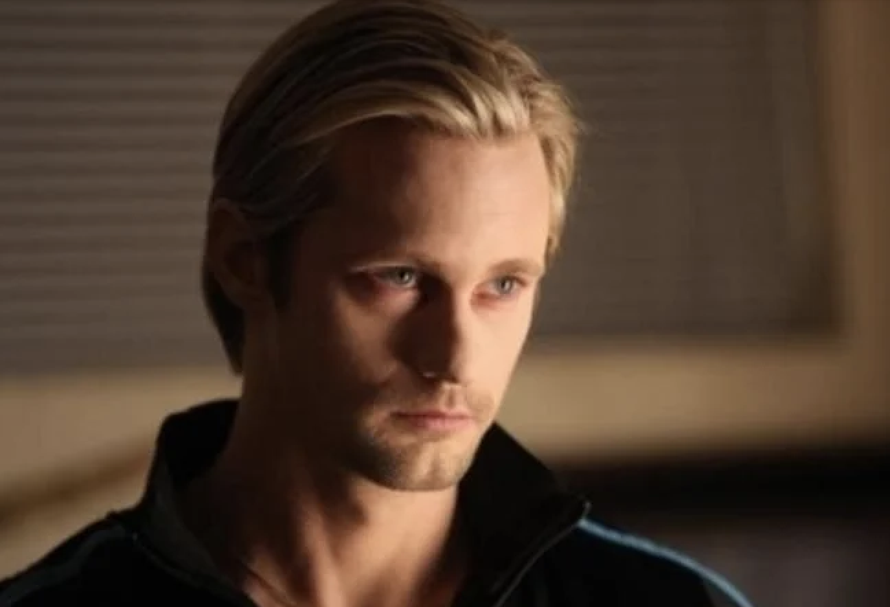 A man gazes off-camera with a serious expression, wearing a dark collared shirt. The background is out of focus