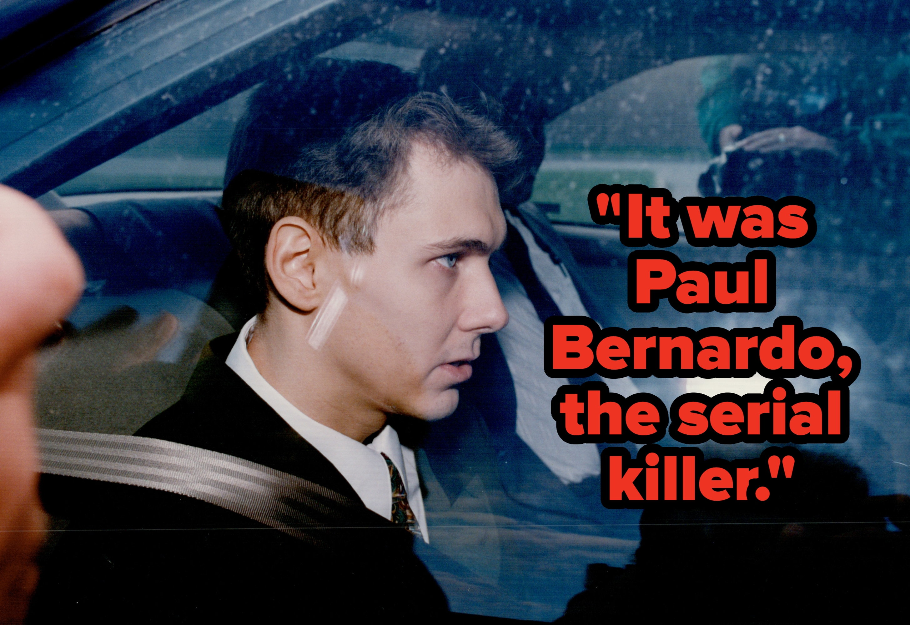 Serial killer Paul Bernardo wearing a suit, seated in a car with a seatbelt on