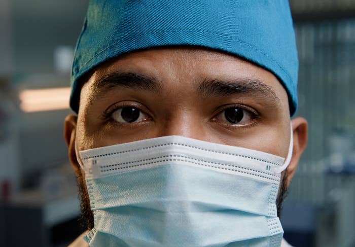 A healthcare worker wears a surgical mask and cap, focusing intently